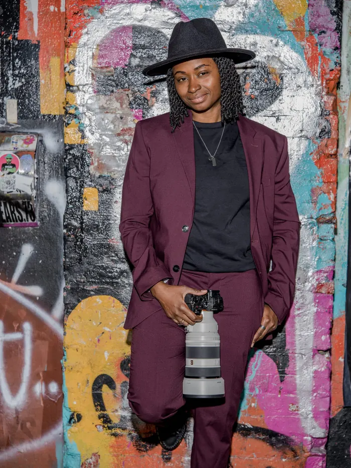 Kash posing with one knee up against a graffiti-covered wall