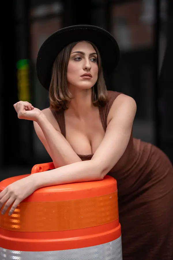 Woman in a black hat leaning on an orange traffic barrel