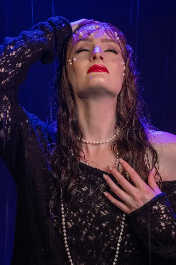 Woman in black lace and pearls under violet light