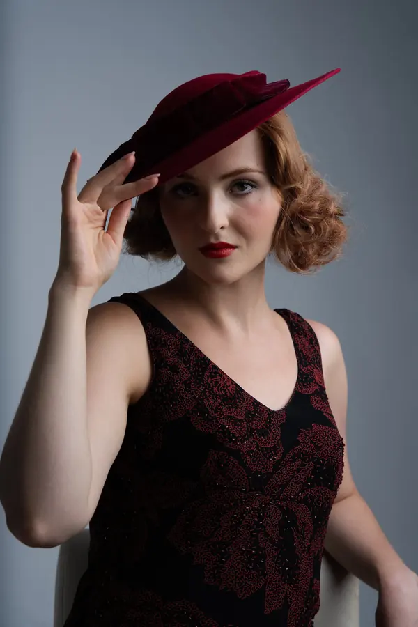 Portrait of a woman in a burgundy hat and lace dress on a grey backdrop