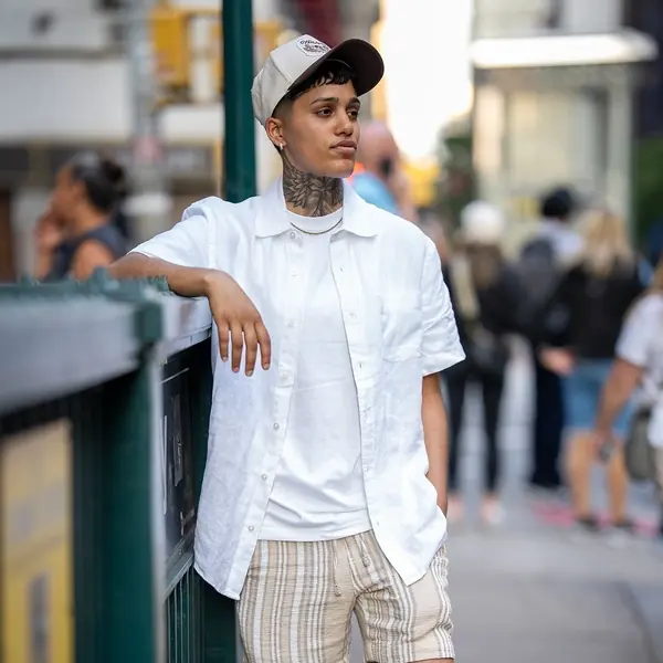 Tattooed woman in a white shirt leaning on a railing downtown